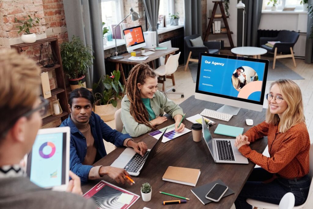 A diverse team at a programmatic advertising agency collaborates around a table with laptops, tablets, and performance charts in a modern office.