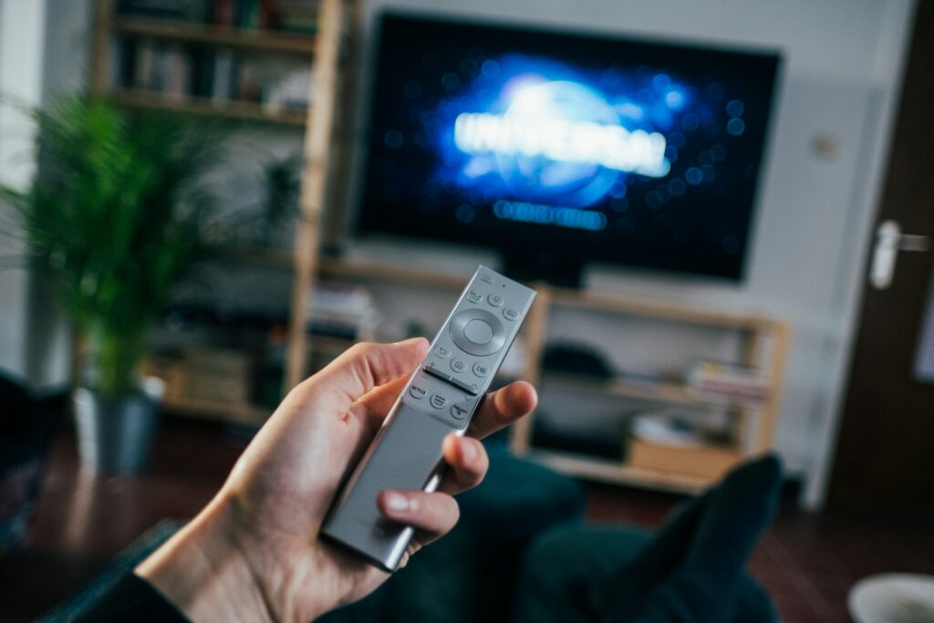A viewer holding a TV remote in front of a connected TV screen illustrates what is CTV: streaming content delivered through internet-connected televisions.