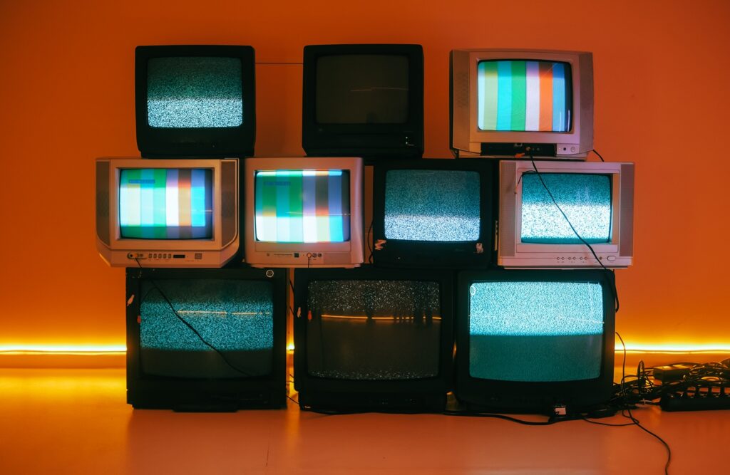 Stacked vintage CRT televisions displaying static and color test bars against an orange-lit wall, illustrating what is programmatic tv buying.