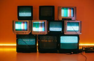 Stacked vintage CRT televisions displaying static and color test bars against an orange-lit wall, illustrating what is programmatic tv buying.