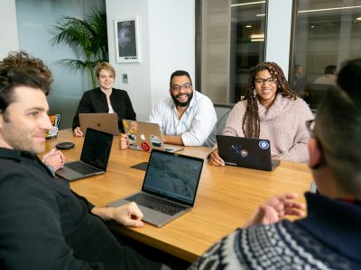 A diverse marketing team collaborating on programmatic ad buying strategy during a conference room meeting with laptops open.