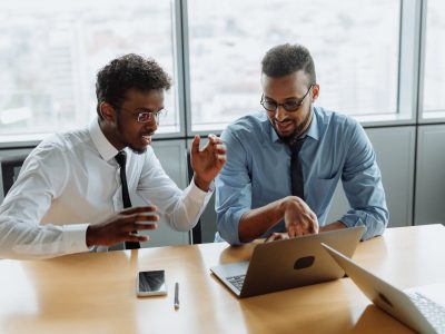 Two media buyers reviewing PMP advertising campaign performance on a laptop in a modern office setting.
