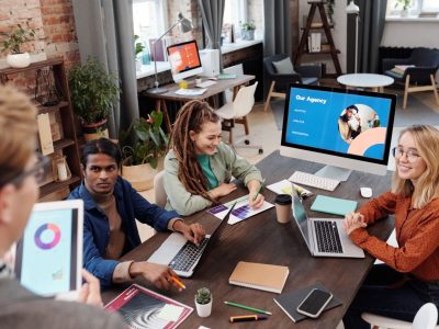 A diverse team at a programmatic advertising agency collaborates around a table with laptops, tablets, and performance charts in a modern office.