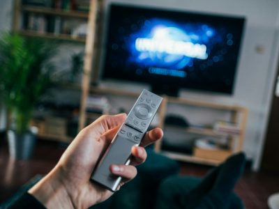 A viewer holding a TV remote in front of a connected TV screen illustrates what is CTV: streaming content delivered through internet-connected televisions.