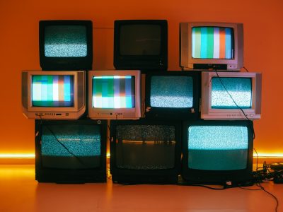 Stacked vintage CRT televisions displaying static and color test bars against an orange-lit wall, illustrating what is programmatic tv buying.